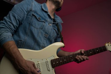 Kot ceketle beyaz elektro gitar çalan bir adam.