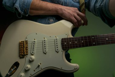 Kot ceketle beyaz elektro gitar çalan bir adam.