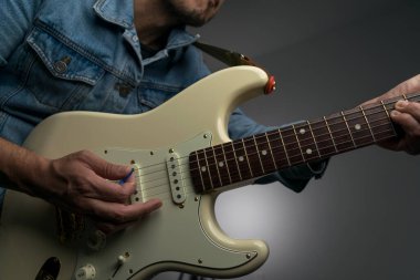 Kot ceketle beyaz elektro gitar çalan bir adam.