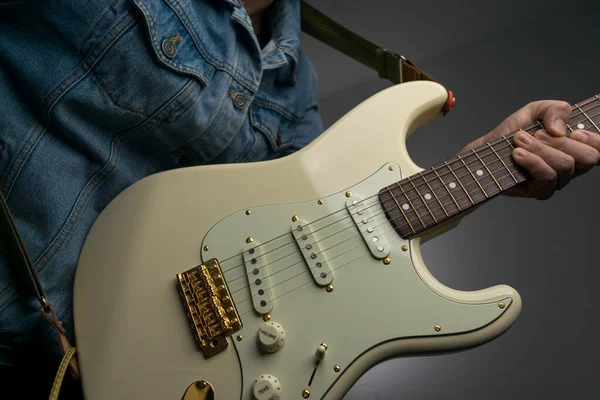 Kot ceketle beyaz elektro gitar çalan bir adam.