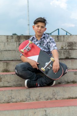 Mavi beyaz kaykay tişörtü, siyah yırtık kot pantolon, siyah paten ayakkabısı giyen Kolombiya 'nın Bogota kaykay parkında harika saç kesimi olan yakışıklı Asyalı bir çocuğun sokak fotoğrafı.