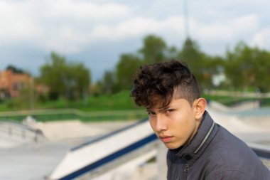 Açık yeşil gözlü, genç, yakışıklı bir İspanyol 'un portresi. Bogota, Kolombiya' da kaykay parkında gri bir ceket giyen harika bir saç kesimi.