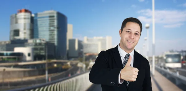 Empresário sorrindo e sentindo-se feliz entregando polegares com Business City e edifícios corporativos em segundo plano — Fotografia de Stock