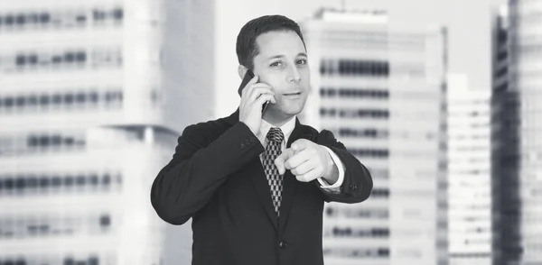 Businessman Talking On The Phone And Pointing Index Finger Towards Camera With Business City and Corporate Buildings In Background — Stock Photo, Image
