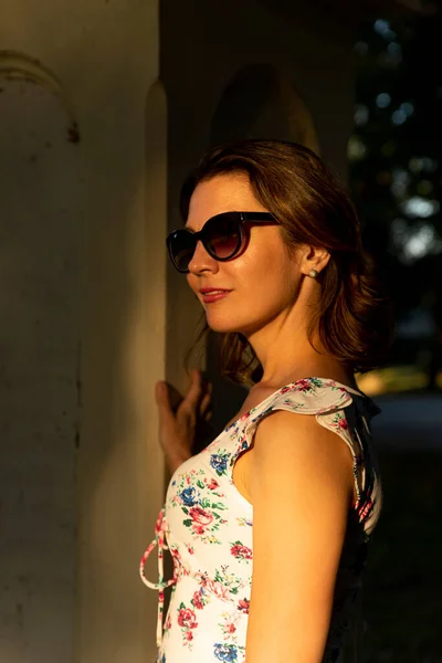 Beautiful woman in flower dress wearing sunglasses at sunset. Beauty and Fashion luxury style. Golden hour photo