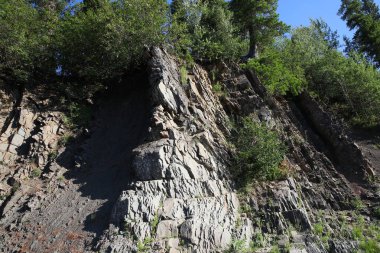 Kayalık dağ yamacında çatlaklar ve tepesinde yemyeşil bitki örtüsü olan çıkıntılar. Rusya 'nın Ural Dağları' ndaki kaya şistinin dokusu..