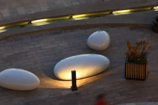 Outdoor terrace decor with lighting in a modern style.Wooden flowerpot with flowers stones benches glow in the place of rest at dusk in a light fog.The view from the top of the Botanical design.