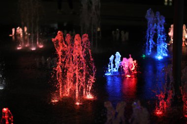 Gece çeşmesi. Siyah üzerine renkli bir şelale çağlıyor. Kırmızı mavi güçlü jet basıncı. Soyut arka plan.