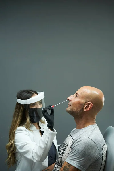 Virus Swab Test. Female doctor doing a nasopharyngeal swab test to a male patient. The doctor wearing medical protective equipment: mask, protective glasses, gloves and smock.