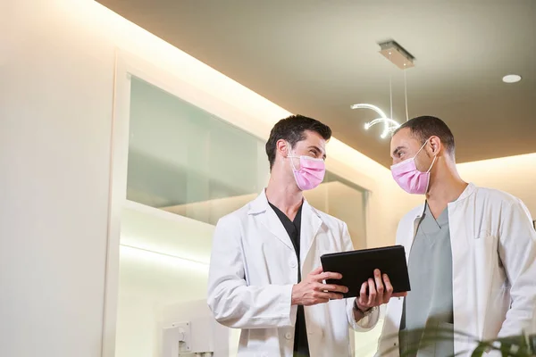 Two doctors in a mask commenting on the results with a tablet in hand. Gynecological, dental or aesthetic clinic. Medical concept.