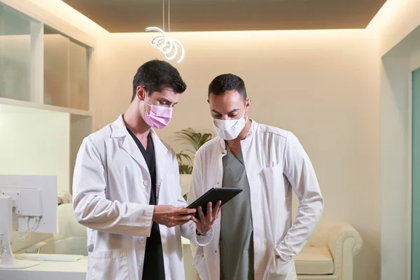 Two doctors with masks looking at the tablet screen in a gynecological, dental or aesthetic clinic.