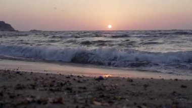 Denizde güzel bir gün batımı, denizin kumlu kıyılarında bir dalga akıyor, yakınlarda..