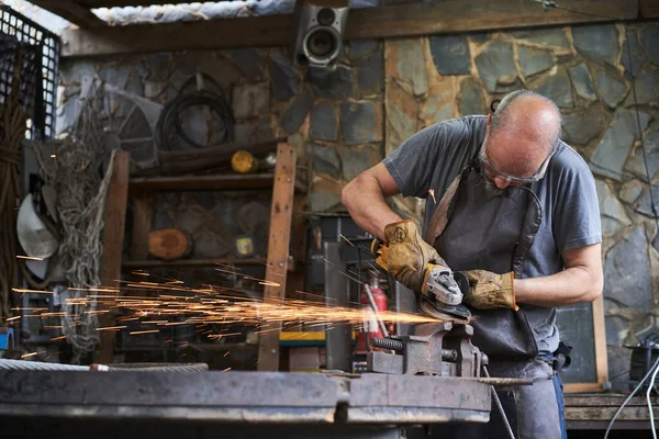Worker cutting with a grinder in an old blacksmith shop. It is equipped with safety glasses and gloves