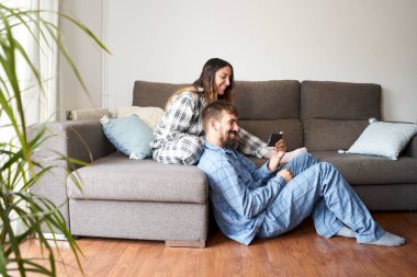 Evde pijama giymiş seyyar seyyar gezen genç bir çift. Tatilde mutlular ve gülüyorlar, birlikte olmanın tadını çıkarıyorlar..