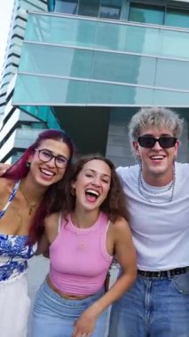 Dikey. Beş neşeli çoklu etnik öğrenci birbirine sarılıyor ve gülümsüyor, güneşli bir günde şehirde birlikte eğleniyorlar, barış işareti yapıyorlar.