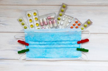 Maske ve tabletlerle bembeyaz ahşap arka planda medikal düz yatak. Tıbbi konsept. Üst görünüm.