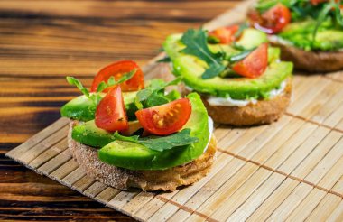 Avokado püresi ve taze dilimlenmiş domatesler kahverengi ahşap zemin üzerinde ızgara tost ekmeği. Güzel ve sağlıklı bir kahvaltı. Sağlıklı ve lezzetli yemekler..