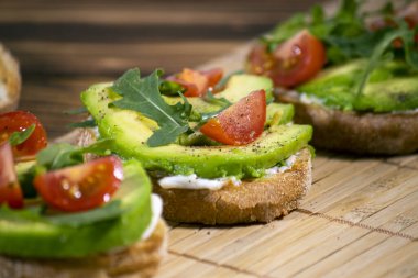 Avokado püresi ve taze dilimlenmiş domatesler kahverengi ahşap zemin üzerinde ızgara tost ekmeği. Güzel ve sağlıklı bir kahvaltı. Sağlıklı ve lezzetli yemekler..