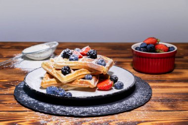 Üzerinde böğürtlen, böğürtlen, çilek ve ahşap zemin üzerinde yabanmersini bulunan Belçika wafflelarının yakın görüntüsü