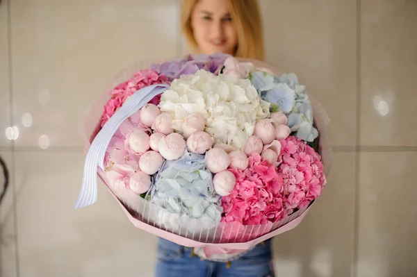Girl in pink shirt holding in her hands a beautiful bright big bouquet of pink, blue and white flowers decorated with a bow