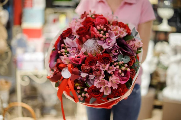 Florist holding a large bright bouquet in red tones consisting of roses and other beautiful flowers in a flower shop