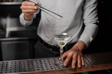 Bir zeytin trasparent alkollü içki çubuğu ile boş martini cam içine ekleme barmen sayaç