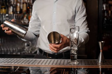 Barmen çubuğundaki boş bir çelik kokteyl shaker holding beyaz gömlekli sayaç üzerinde arka plan bulanık