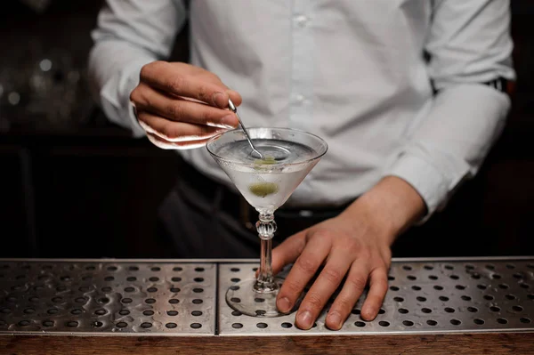 白いシャツのあふれるバーをアルコール飲料とマティーニ グラスにオリーブを追加するバーテンダー カウンター — ストック写真