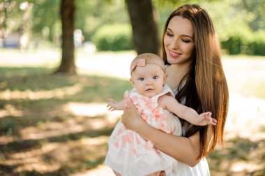 Genel arka plan bulanık parkta genç esmer anne küçük sarışın kızı tutan eller