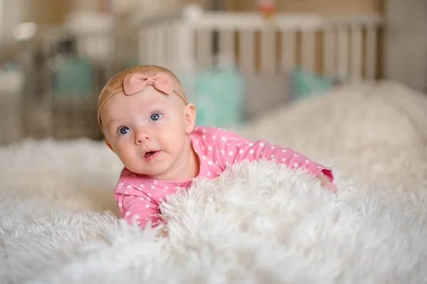 Little blue eyes girl with a bow on her head lying on the white cozy bed in the domestic room