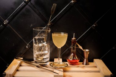 Buz, sarı kokteyl, tweezzers ve syrop siyah arka plan üzerine ahşap stand ile ölçüm fincan