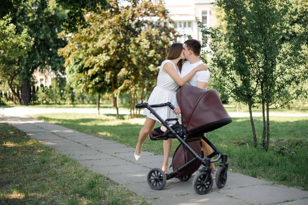 Happy parents kissing near their little daughter in the babby carriage in the public park