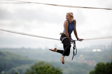 Yan görünümü kız slackline üzerinde oturan ve ağaçlar ve berrak gökyüzü arasında evlerin zemin üzerine geri arıyorsunuz