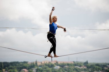 Genç Sarışın kadın ayakta kaldırdı tek kollu ve berrak gökyüzü arka plan üzerinde slackline üzerine diğer