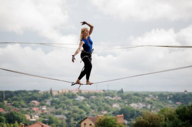 Genç Sarışın kadın ayakta elleri açık gökyüzü arka planda slackline üzerinde doğru yönde hareket ettirildiğinde