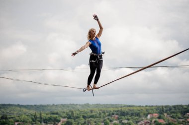 Genç Sarışın kadın Dengeleme elleri açık gökyüzü arka planda slackline üzerinde doğru yönde hareket ettirildiğinde