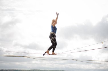 Açık gökyüzü arka plan üzerinde mesafe bakarak ve slackline ipe Dengeleme yan görünümü genç sarışın kadın