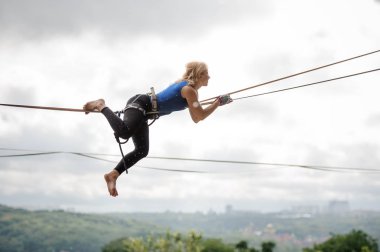 Açık gökyüzü arka plan üzerinde mesafe bakarak ve slackline ipe yalan yan görünümü genç sarışın kadın