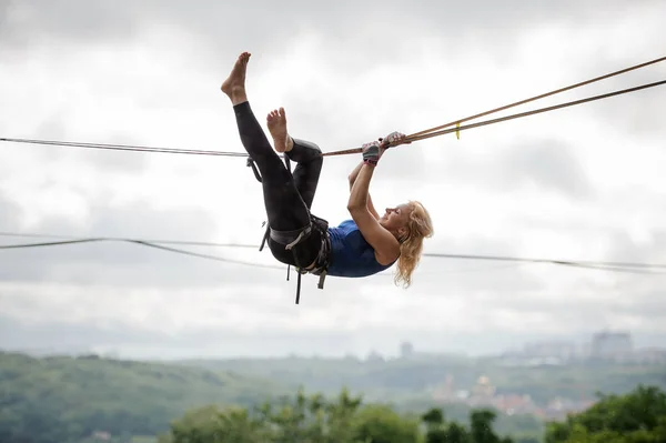 Young blondie woman hanging on the slackline upside down on the background of clear sky