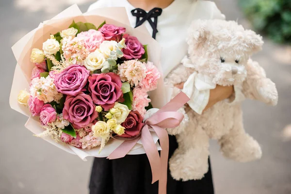 School girl dressed in school uniform holding a bright colorful festive bouquet and teddy bear — Stock Photo, Image