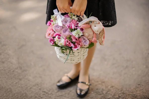 Ragazza della scuola che tiene un simpatico cesto di vimini pieno di fiori rosa brillante decorato con un coniglio giocattolo — Foto Stock