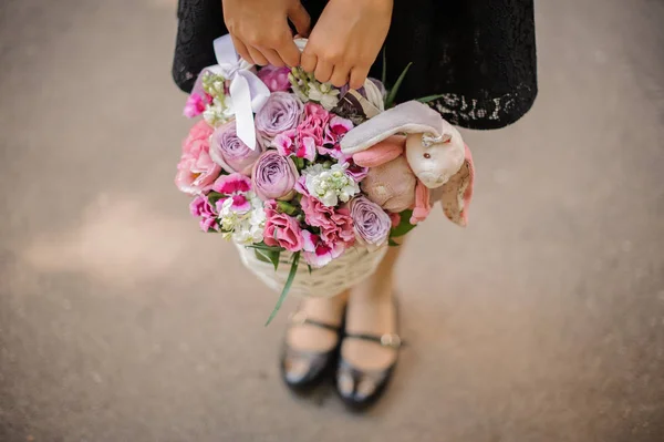 Menina segurando uma cesta de vime bonito cheio de flores rosa brilhante decorado com um coelho de brinquedo — Fotografia de Stock