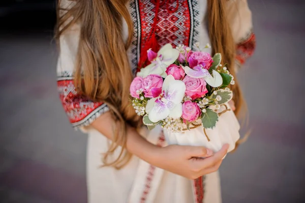 Lång haired kvinna i nationella ukrainska blus broderi håller en söt vit kruka med rosa och röda rosor — Stockfoto