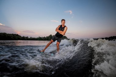 Genç wakesurfer yaz günbatımında günbatımı gökyüzü karşı elleri geçiş nehir dalgaları aşağı sürme