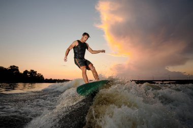 Genç adam wakesurfing nehir dalgaları akşam güzel bulutlu gökyüzü arka plan üzerinde aşağı