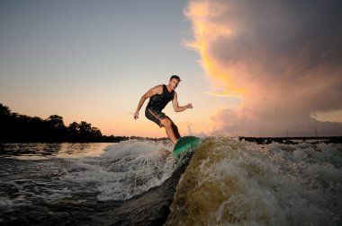 Etkin adam wakesurfing nehir dalgaları akşam güzel bulutlu gökyüzü arka plan üzerinde aşağı