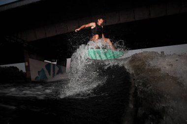 Nehir dalgalara karşı köprü aşağı yaz akşamı sürme mutlu aktif ve Genç wakesurfer