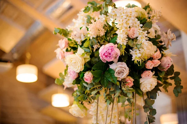 Wedding decor bouquet of tender pink peonies and roses with green leaves under the ceiling on the blurred background