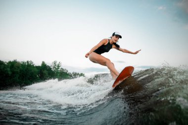 Genç çekici esmer kız portakal wakesurf Motorbot ağaçlar arka plan üzerinde yüksek dalga sürme