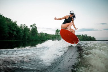 Genç esmer kadın Motorbot ağaçlar arka plan üzerinde yüksek dalga üzerinde turuncu wakesurf atlama
